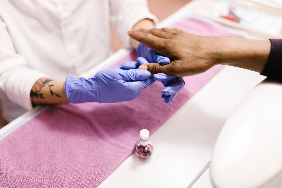 A nail technician applying cuticle oil onto a client's nails
